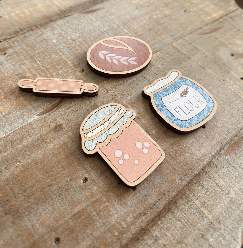 Puede incluir: Recortes de madera con tem&aacute;tica de reposter&iacute;a, que incluyen un rodillo con lunares, una hogaza de pan con trigo, un tarro de harina y un tarro con un dise&ntilde;o floral. Los art&iacute;culos son en tonos marr&oacute;n, rosa y azul, sobre un fondo de madera.