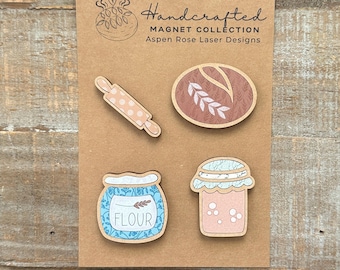 May include: A set of four handcrafted wooden magnets on a brown card. The magnets include a rolling pin, a loaf of bread, a jar of flour, and a jar of jam. The magnets have a rustic, farmhouse style.