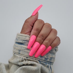 Könnte beinhalten: Ein Handmodell trägt eine Jeansjacke mit langen, leuchtend pinken, mandelförmigen Press-on-Nägeln.