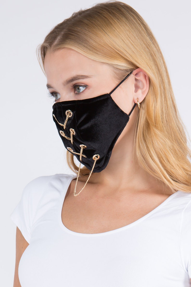 May include: Black velvet face mask with gold chain detail and metal eyelets. The mask has a criss-cross chain design.