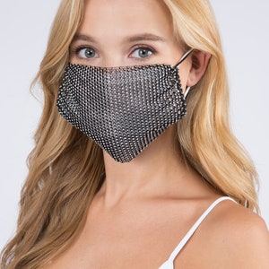 May include: A silver sparkly face mask with a mesh design. The mask is worn by a person with long blonde hair.