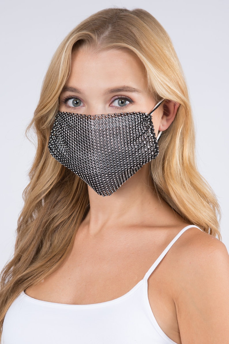 May include: A silver sparkly face mask with a mesh design. The mask is worn by a person with long blonde hair.