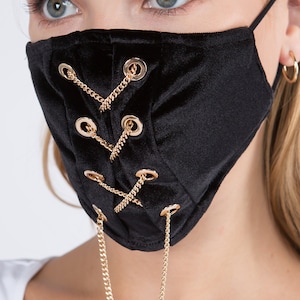 May include: Black velvet face mask with gold chain and eyelets. The mask has a lace-up design with gold chains attached to the eyelets.