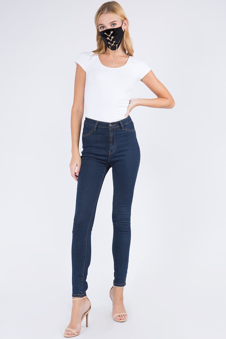 May include: A woman wearing a black velvet face mask with gold chain detailing. The mask has a lace-up design. She is wearing a white t-shirt and dark blue jeans.