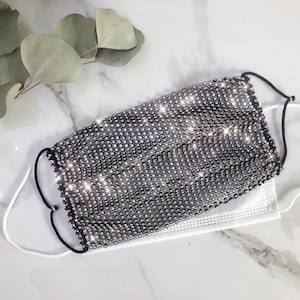 May include: A black face mask covered in silver rhinestones. The mask has elastic ear loops.
