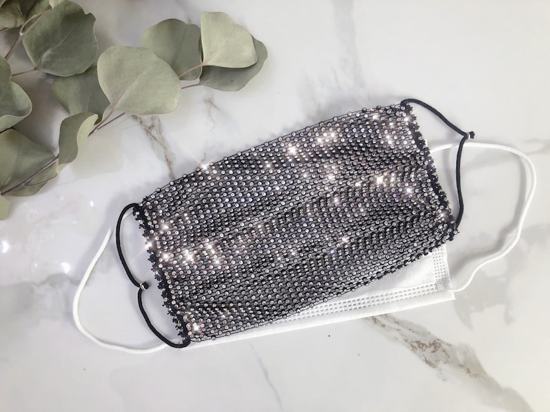 May include: A black face mask covered in silver rhinestones. The mask has elastic ear loops.
