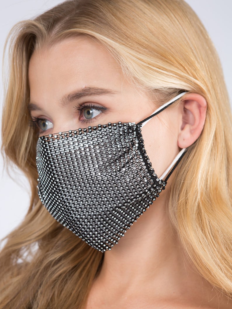 May include: A black face mask with a silver rhinestone mesh design. The mask has elastic ear loops.