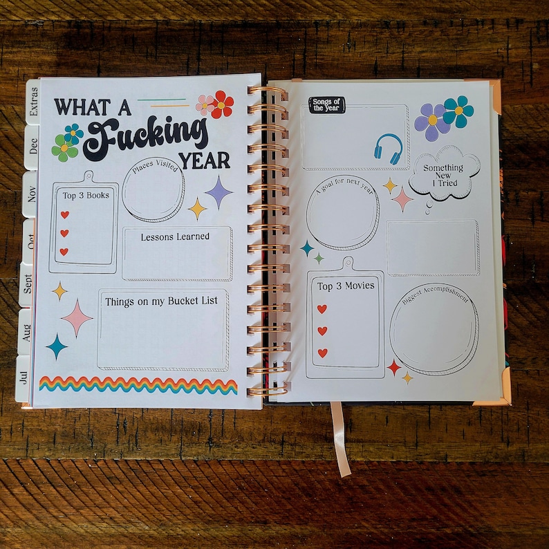 May include: A colorful planner with the words "What a Fucking Year" on the cover. The planner has sections for "Top 3 Books", "Places Visited", "Lessons Learned", "Things on my Bucket List", "Songs of the Year", "A Goal for Next Year", "Something New I Tried", "Top 3 Movies", and "Biggest Accomplishment".