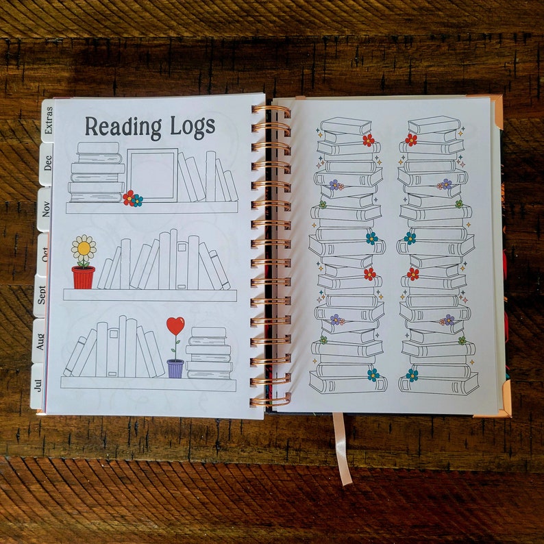 May include: A white reading log book with a pink, orange, and purple color scheme. The cover features the text "Reading Logs" and illustrations of bookshelves with books. The book has a spiral binding and a ribbon bookmark.