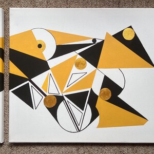 Peut inclure: Tableau abstrait g&eacute;om&eacute;trique sur toile avec un design audacieux. L'&oelig;uvre pr&eacute;sente des formes noires, blanches et dor&eacute;es, notamment des triangles, des cercles et des lignes. La toile est tendue et pr&ecirc;te &agrave; &ecirc;tre accroch&eacute;e, ajoutant une touche moderne &agrave; tout espace.