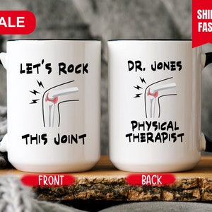 May include: White ceramic coffee mug with a black rim and handle. The front of the mug has a cartoon knee with lightning bolts and the text "Let's Rock This Joint". The back of the mug has the text "Dr. Jones Physical Therapist".