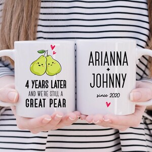 Puede incluir: Dos tazas blancas con texto negro y un dise&ntilde;o de pera. La taza de la izquierda dice "4 a&ntilde;os despu&eacute;s y seguimos siendo una gran pera". La taza de la derecha dice "Arianna + Johnny desde 2020".