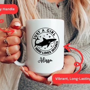 May include: White ceramic mug with a black shark graphic and the text "JUST A GIRL WHO LOVES SHARKS" and the name "Alissa". The mug has a sturdy handle and a vibrant, long-lasting print.