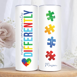 May include: Two white stainless steel tumblers with a colorful puzzle piece design. One tumbler says "everyone communicates DIFFERENTLY" with a heart-shaped puzzle piece. The other tumbler has four puzzle pieces with the words "advocate", "love", "accept", and "adopt" and the name "Mason" at the bottom.