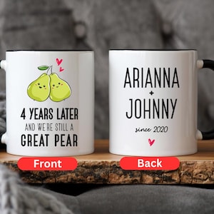 Puede incluir: Taza de cer&aacute;mica blanca con asa y borde negros. La parte delantera de la taza presenta una imagen de dibujos animados de dos peras con el texto "4 Years Later and We're Still a Great Pear". La parte posterior de la taza tiene el texto "Arianna + Johnny since 2020".
