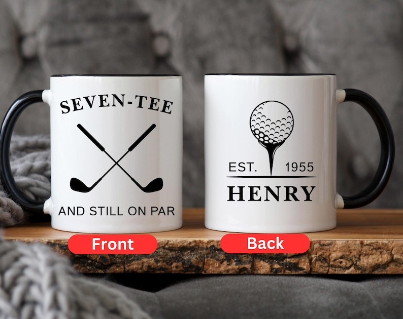 May include: White ceramic mug with a black handle and rim. The front of the mug features the text "SEVEN-TEE" above crossed golf clubs and "AND STILL ON PAR". The back has a golf ball graphic, the text "EST. 1955 HENRY".