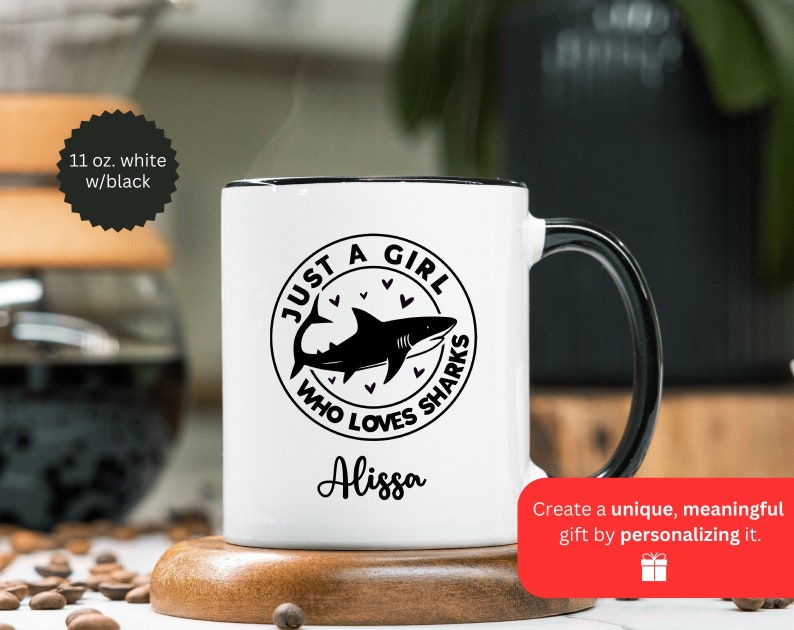 May include: White ceramic mug with a black handle and rim. The mug features a black graphic of a shark inside a circle with the text "JUST A GIRL WHO LOVES SHARKS" and the name "Alissa". The mug is 11 oz.