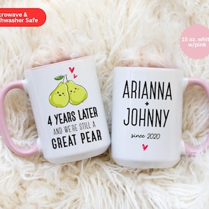 Puede incluir: Dos tazas de cer&aacute;mica blanca con asas rosas. Una taza tiene un dise&ntilde;o de pera y el texto "4 a&ntilde;os despu&eacute;s y seguimos siendo una gran pera". La otra taza tiene el texto "Ariana + Johnny desde 2020".