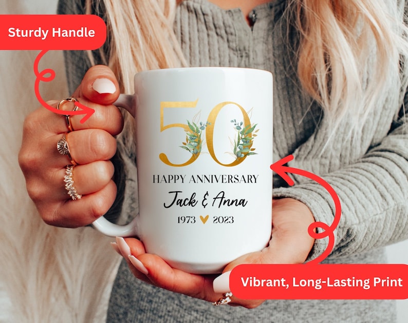 May include: White ceramic mug with a gold 50th anniversary design, featuring a floral motif and the text "Happy Anniversary Jack & Anna 1973 &hearts; 2023".
