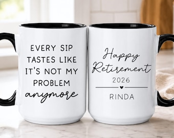Puede incluir: Dos tazas de cerámica blanca con asas y bordes negros. La taza de la izquierda tiene el texto en negro: EVERY SIP TASTES LIKE IT'S NOT MY PROBLEM anymore. La taza de la derecha tiene el texto en negro: Happy Retirement 2026, un corazón y RINDA.