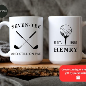 May include: Two white ceramic golf mugs. One mug features crossed golf clubs with the text "SEVEN-TEE AND STILL ON PAR." The other mug has a golf ball design with "EST. 1955 HENRY." Each mug is 15 oz.