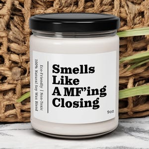 May include: A white candle jar with a black lid. The label reads "Smells Like A MF'ing Closing" and "Eco-Friendly | Non-Toxic 100% Natural Soy Wax Blend 9oz".
