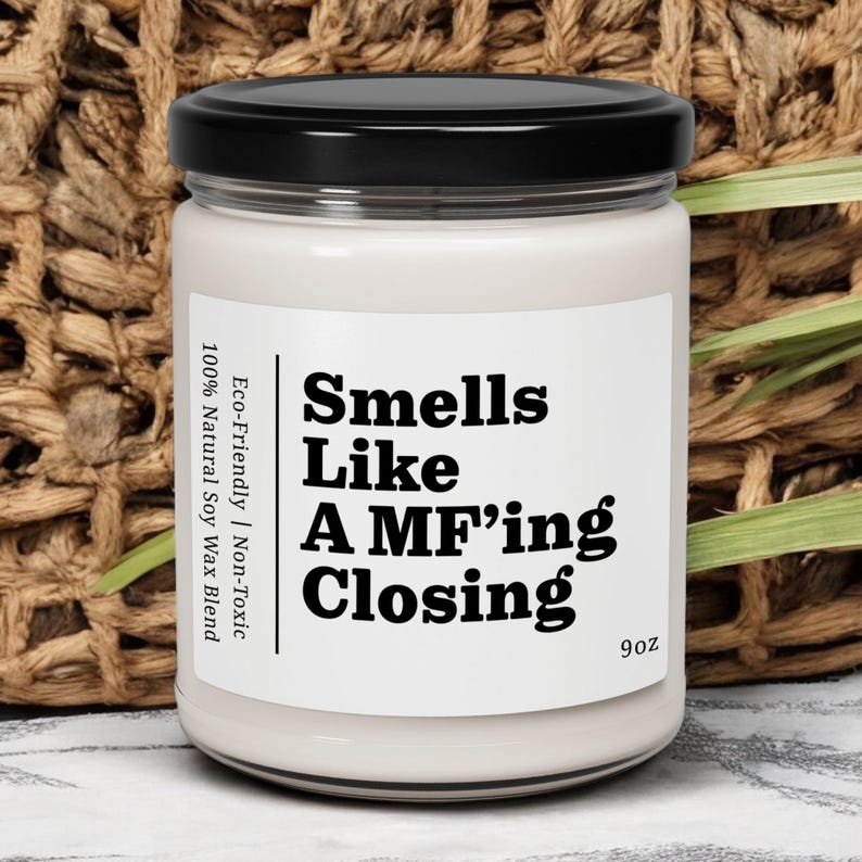 May include: A white candle jar with a black lid. The label reads "Smells Like A MF'ing Closing" and "Eco-Friendly | Non-Toxic 100% Natural Soy Wax Blend 9oz".