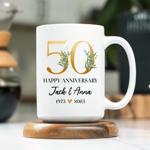 May include: White ceramic mug with a gold 50 and floral design. The mug says "Happy Anniversary Jack & Anna 1973 &hearts; 2023".