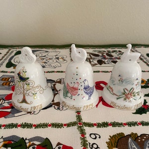 May include: Three white porcelain Christmas bells with gold trim and colorful painted designs. The bells are dated 1973, 1975, and 1979.