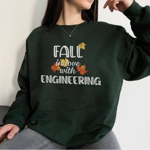 May include: A dark green sweatshirt with the text "Fall in love with Engineering" in white lettering. The text is surrounded by three small orange and yellow leaf illustrations.