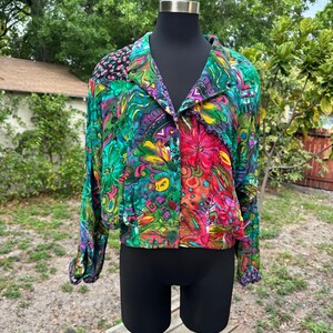 May include: A colourful, abstract patterned button-up shirt with long sleeves. The shirt is green, pink, blue, yellow, and purple.