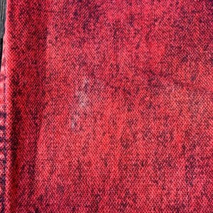 May include: Close-up of a textured fabric with a red and black speckled pattern. The fabric has a woven appearance, with the red color dominating and the black speckles creating a contrasting effect. The texture appears slightly rough.