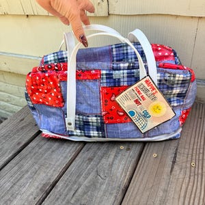 May include: A patchwork picnic bag with white handles. The bag features a mix of red paisley, blue plaid, and denim-like fabrics. A tag reads "Nappe's Insulated Picnic Bag, Helps Keep Food Hot or Cold."