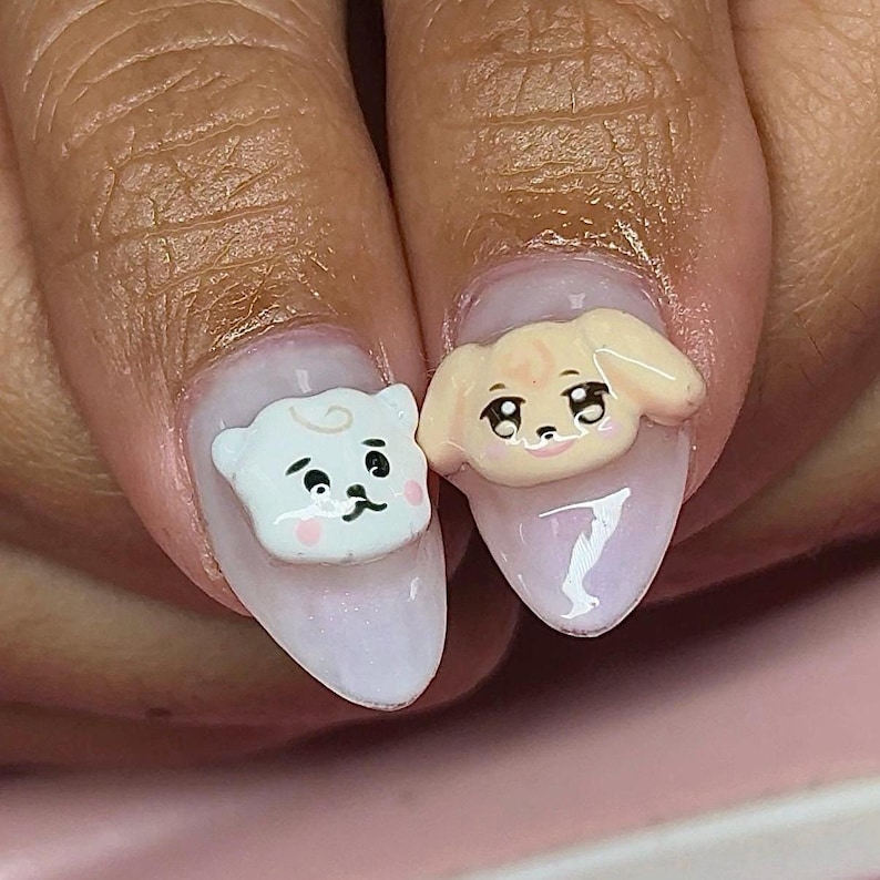 Puede incluir: Primer plano de dos u&ntilde;as manicuradas con arte de u&ntilde;as de animales de dibujos animados en 3D. Una u&ntilde;a presenta un oso blanco, la otra un perro canela. Ambos tienen ojos negros y mejillas rosadas, sobre una laca de u&ntilde;as rosa claro.