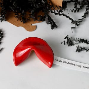 May include: A red ceramic fortune cookie with a white paper slip that reads "Happy 9th Anniversary! xoxo".