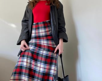 Puede incluir: Una mujer con un top rojo, una chaqueta de cuero negra y una falda de cuadros. Lleva un bolso tote negro.