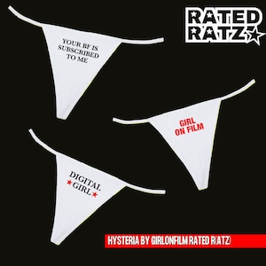 May include: Three white thongs with different phrases printed on them. The phrases are "Your BF is Subscribed to Me", "Girl on Film", and "Digital ★Girl★". The thongs are arranged in a triangle shape with the top thong pointing upwards. The background is black.
