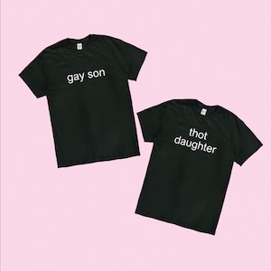 May include: Two black t-shirts with white text. The first shirt says "gay son" and the second shirt says "thot daughter".