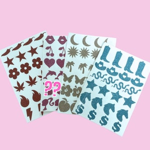 Op de afbeelding: Vier vellen met stickers met verschillende ontwerpen. De eerste vel heeft rode en bruine glitterontwerpen, waaronder een bloem, een ster, een bliksem en een blad. De tweede vel heeft roze en rode glitterontwerpen, waaronder een hart, een kers, een dolfijn en een vlinder. De derde vel heeft gouden glitterontwerpen, waaronder een zon, een halve maan, een palmboom en een appel. De vierde vel heeft blauwe glitterontwerpen, waaronder een slang, een cowboylaars, een ster en een dollar.