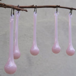 May include: Five pink glass teardrop ornaments hanging from a branch. The ornaments are all the same size and shape, and they are hanging from a thin wire.
