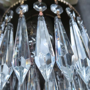 May include: Close-up of a chandelier with multiple crystal prisms hanging from a metal frame. The prisms are clear and reflect light.