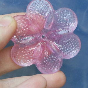 May include: A pink glass flower with a textured surface. The flower has five petals and a hole in the center.