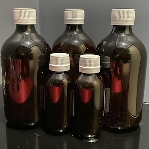 May include: Four amber glass bottles with white lids. The bottles are of different sizes and are arranged in a row from largest to smallest.