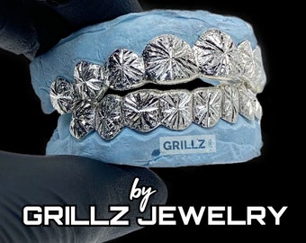 Może przedstawiać: Srebrne grillz z diamentowym wzorem. Grillz są prezentowane w formie odlewu ust. Tekst "GRILLZ" jest widoczny na formie.