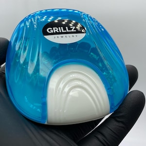 以下が含まれることがあります： 前面に「GRILLZ JEWELRY」という文字が書かれた、白い内装の青いプラスチックケースです。