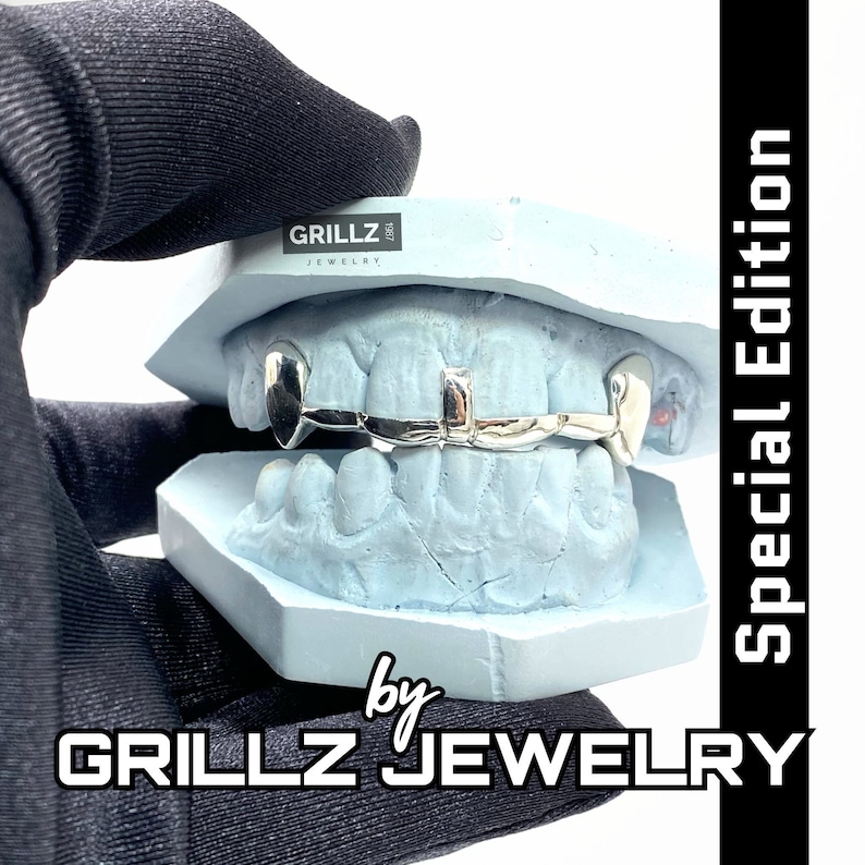 K&ouml;nnte beinhalten: Ein silberner Grillz mit einem diamantf&ouml;rmigen Mittelst&uuml;ck und zwei Fangz&auml;hnen auf jeder Seite. Der Grillz wird in einer blauen Form gezeigt. Der Text "GRILLZ JEWELRY" ist im Bild sichtbar.