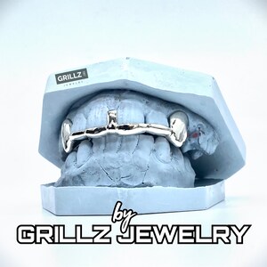 K&ouml;nnte beinhalten: Ein silberner Grillz mit einem einteiligen Balken-Design, in einer blauen Form pr&auml;sentiert. Der Grillz wird von Grillz Jewelry hergestellt.