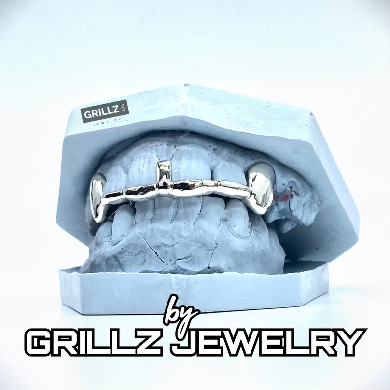K&ouml;nnte beinhalten: Ein silberner Grillz mit einem einteiligen Balken-Design, in einer blauen Form pr&auml;sentiert. Der Grillz wird von Grillz Jewelry hergestellt.