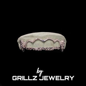 Puede incluir: Grillz de plata con un diseño de corte de diamante. Los grillz están en un molde blanco. El texto "by GRILLZ JEWELRY" está en la parte inferior de la imagen.