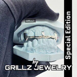 K&ouml;nnte beinhalten: Silberne Grillz mit einem einseitigen Zahndesign, auf einem blauen Zahnmodell ausgestellt. Die Grillz sind mit "Grillz Jewelry" und "Special Edition" gekennzeichnet.